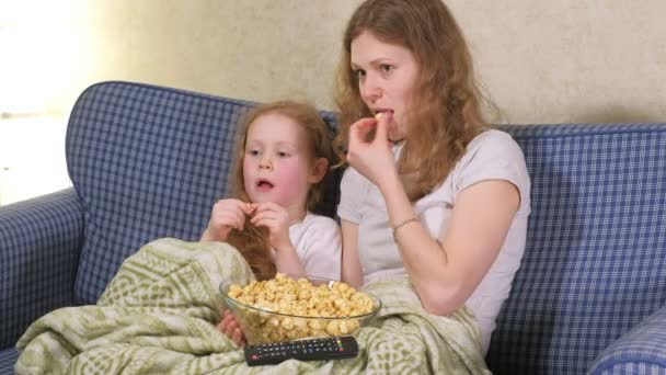 Счастливая семья. Мать и ее дочь девочка едят попкорн на кровати в комнате. перед телевизором — стоковое видео