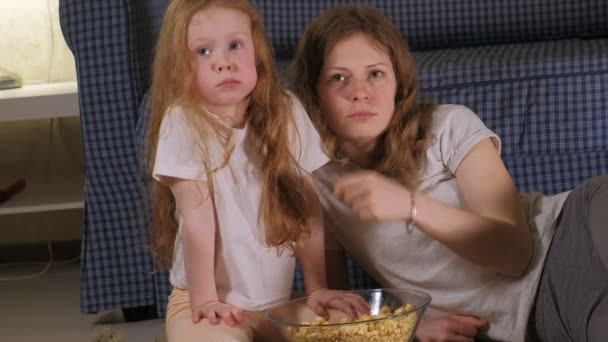 Feliz família amorosa. A mãe e a filha estão a comer pipocas no chão da sala. frente da TV — Vídeo de Stock