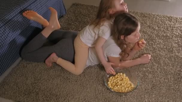 Счастливая семья. Мать с дочерью едят попкорн на полу в комнате. перед телевизором — стоковое видео