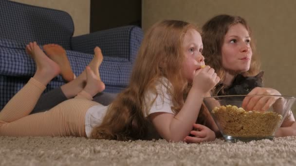幸せな愛情のある家族。母と彼女の娘の子供の女の子は、部屋で床にポップコーンを食べています。テレビの前 — ストック動画