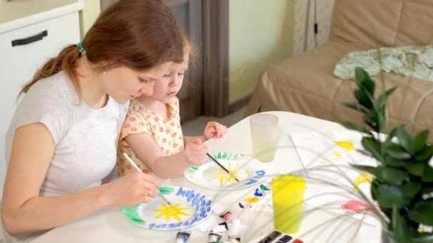 Familia feliz, madre e hija pequeña pintan con pintura en platos blancos — Vídeos de Stock