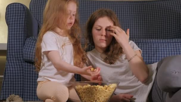 Feliz família amorosa. A mãe e a filha estão a comer pipocas no chão da sala. frente da TV — Vídeo de Stock