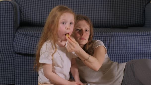 Ευτυχισμένη οικογένεια στην αγάπη. Η μητέρα και το κορίτσι παιδί κόρη τρώνε ποπ κορν στον όροφο στην αίθουσα. μπροστά από την τηλεόραση — Αρχείο Βίντεο