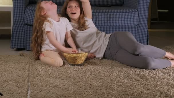 Gelukkige liefdevolle familie. Moeder en haar dochter kind meisje eet popcorn op de vloer in de kamer. vooraan op de Tv — Stockvideo