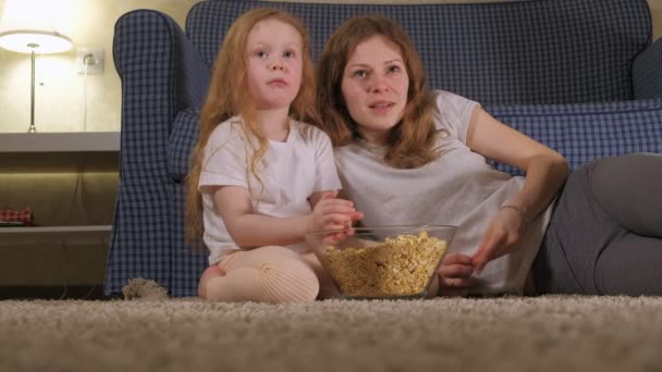 Glückliche liebende Familie. Mutter und Tochter essen Popcorn auf dem Fußboden im Zimmer. vor dem Fernseher — Stockvideo