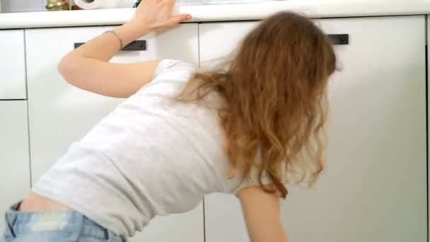 Mujer joven limpieza con plumero en la cocina en casa — Vídeo de stock