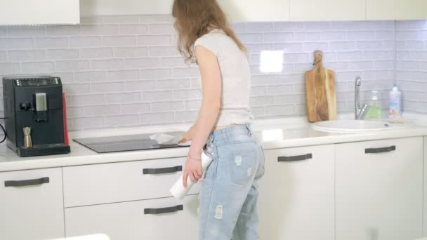 Mujer joven limpieza con plumero en la cocina en casa — Vídeo de stock