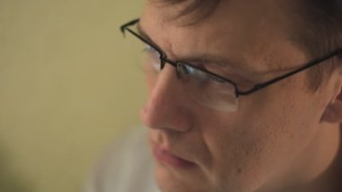 Gözlüklü, bir genç adam kullanarak bir bilgisayar, görünüşe göre çalışmalar. yakın çekim