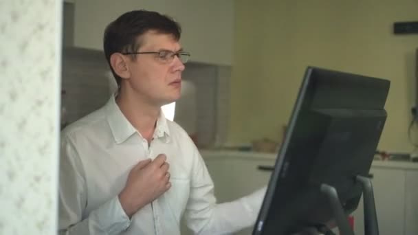 A man unbuttons a button on a white shirt in a stuffy home office during stress — Stock Video