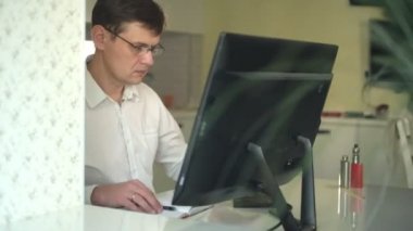 ev ofisinde bir bilgisayar arkasında Beyaz gömlekli bir adam çalışır