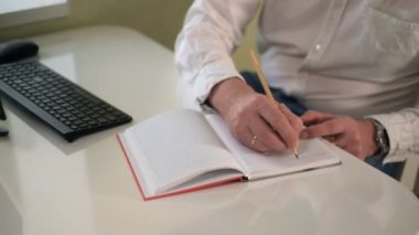 Bir bilgisayarda çalışan iş adamı bir defter bir kalem yakın çekim ile notlar yapma