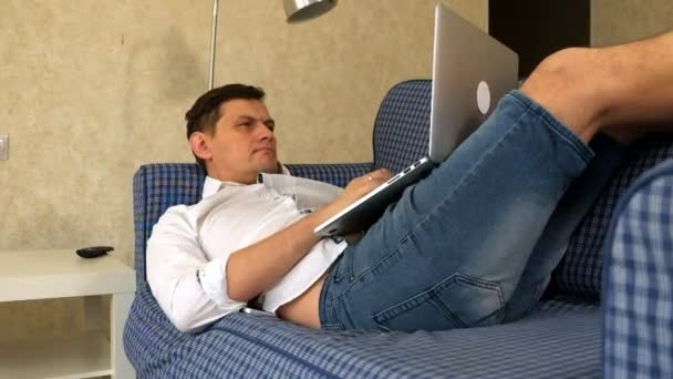 Junger Mann arbeitet ferngesteuert auf Sofa liegend mit Laptop. — Stockvideo