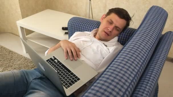 El hombre se quedó dormido mientras trabajaba en el portátil en su sofá en su apartamento de la ciudad — Vídeo de stock