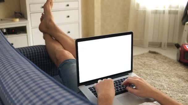 Homem deitado no sofá no quarto trabalhando atrás do laptop — Vídeo de Stock