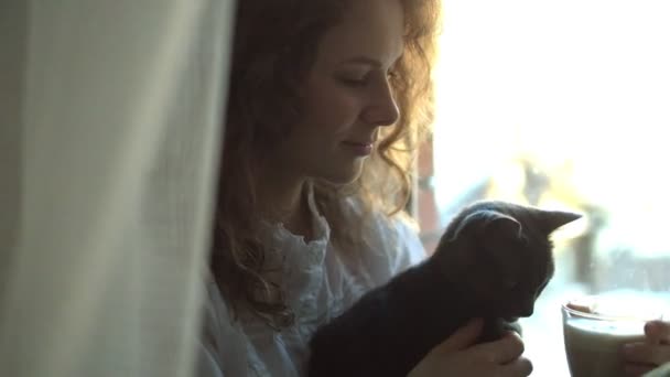 Porträt einer freundlichen Dame, die auf einem Fensterbrett sitzt und Katze mit großer Süße hält. sie schaut und lächelt — Stockvideo