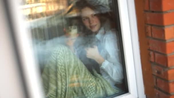 Retrato de la amable dama sentada en el alféizar y sosteniendo al gato con gran dulzura. Ella está mirando y sonriendo — Vídeo de stock