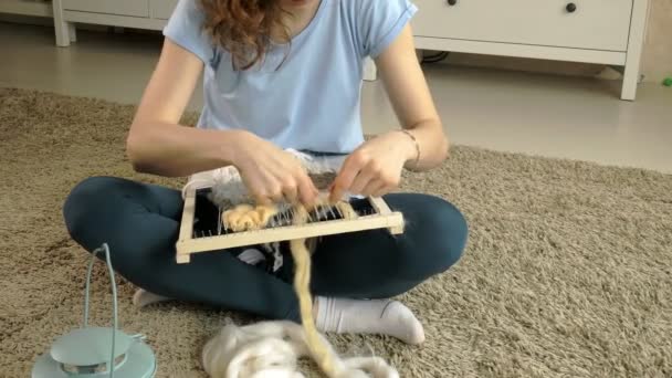 A woman weaves on a loom a beautiful embroidery made of yarn, in a home studio, — Stock Video