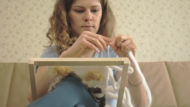 A woman weaves on a loom a beautiful embroidery made of yarn, in a home studio, — Stock Video