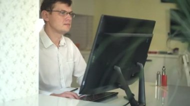 Beyaz gömlekli bir adam frowns, bilgisayar başında ev ofisinde çalışıyor