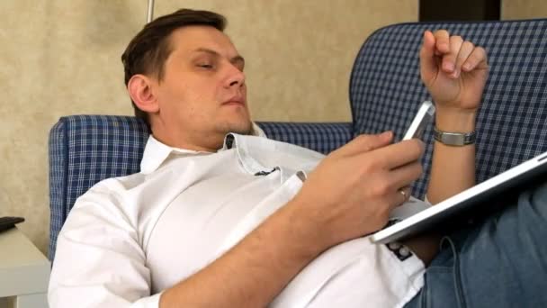 Jeune homme travaillant à distance couché sur un canapé avec ordinateur portable et téléphone — Video