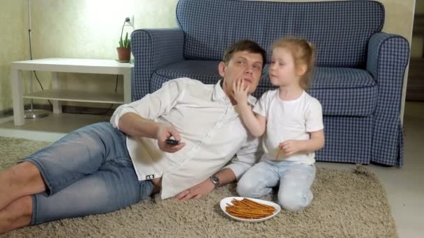 Homem e filha assistindo televisão, sentado no chão comendo lanches — Vídeo de Stock