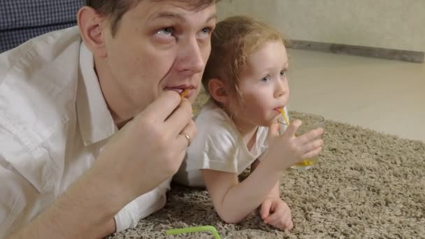 Man och dotter titta på TV, sitter på golvet dricka juice — Stockvideo