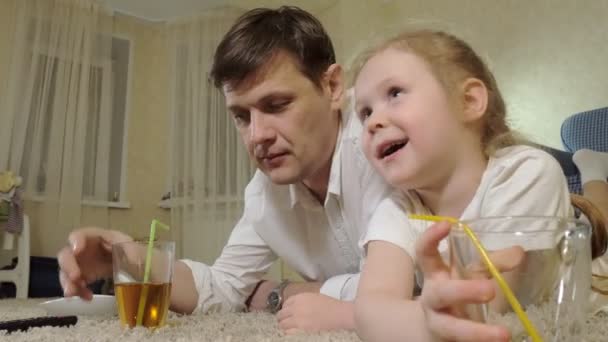 Mann und Tochter fernsehen, auf dem Boden sitzen und Saft trinken — Stockvideo