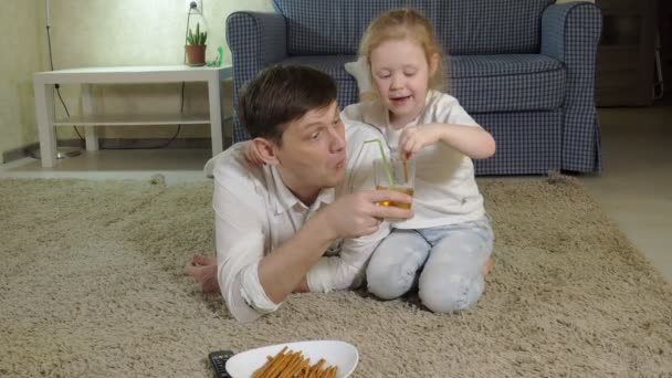 Homem e filha assistindo televisão, sentado no chão comendo lanches — Vídeo de Stock