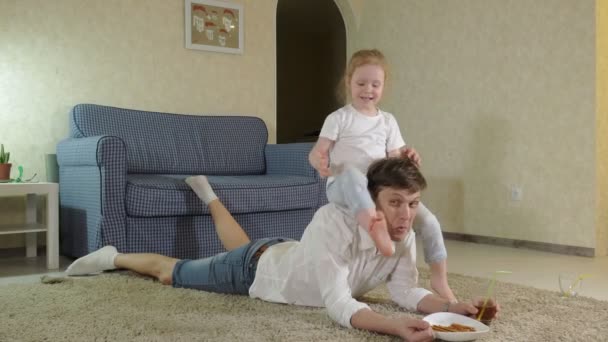 Hombre e hija viendo la televisión, sentados en el suelo comiendo bocadillos — Vídeos de Stock