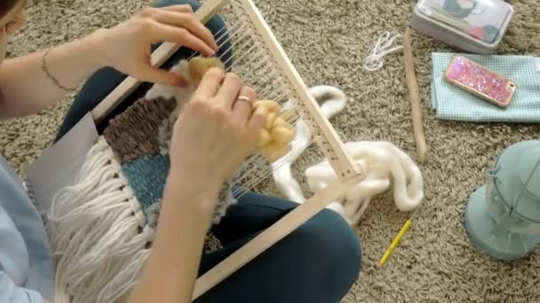 Eine Frau webt auf einem Webstuhl eine schöne Stickerei aus Garn, in einem heimischen Atelier, — Stockvideo