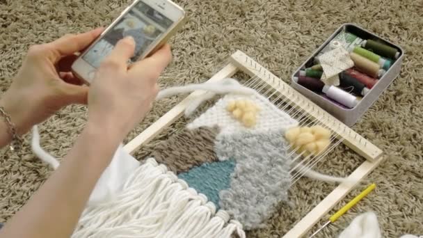 Uma mulher tece em um tear um belo bordado feito de fios, em um estúdio em casa, Fotografias no telefone — Vídeo de Stock