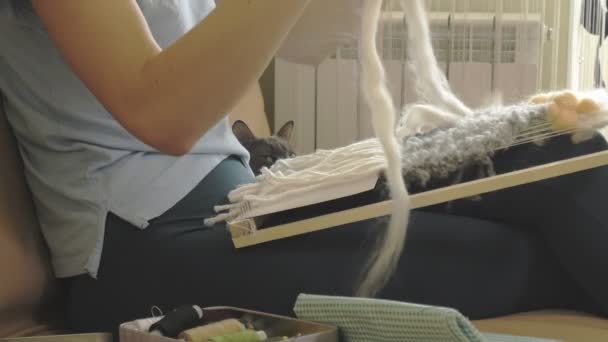 A woman weaves on a loom a beautiful embroidery made of yarn, in a home studio, — Stock Video