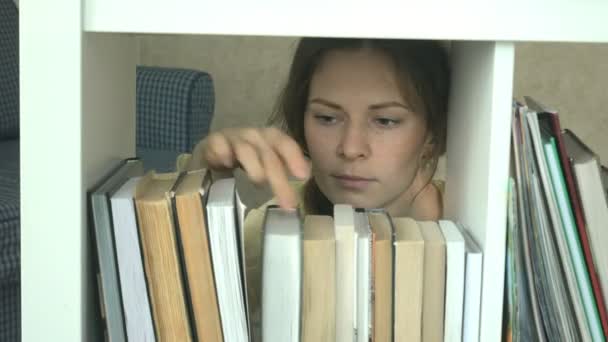 寻找一本书的年轻妇女。学生选择书架库。图书馆女书书架. — 图库视频影像