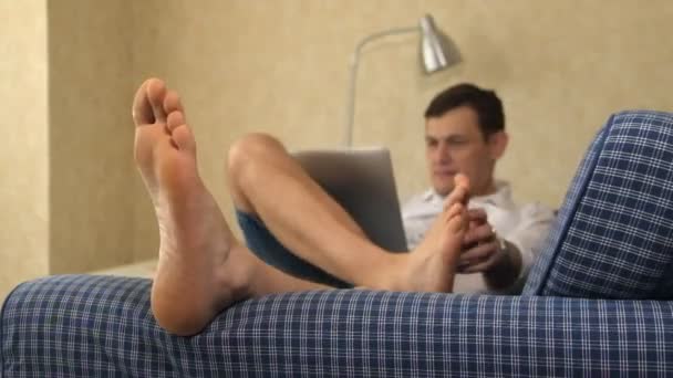 Ernsthafter Geschäftsmann auf dem Sofa liegend, mit Laptop arbeitend, Füße kratzend. Füße, Nahaufnahme — Stockvideo