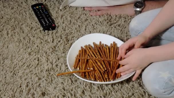 Pria dan anak perempuan menonton televisi, duduk di lantai makan makanan ringan — Stok Video