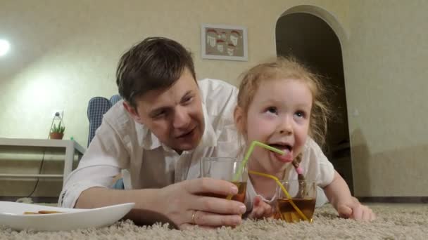 Πιείτε το χυμό άνθρωπος και κόρη παρακολουθώντας τηλεόραση, κάθεται στο πάτωμα — Αρχείο Βίντεο