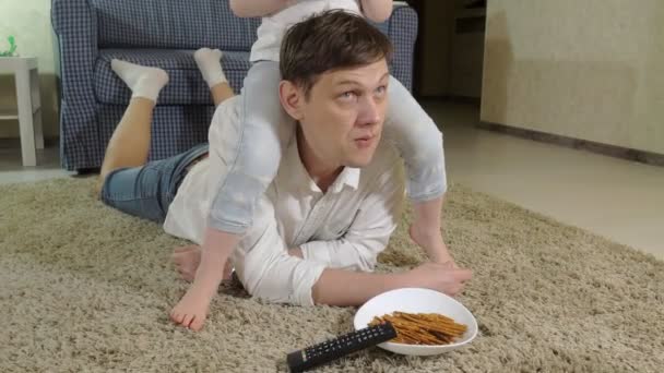 Чоловік і дочка дивиться телевізор, сидячи на підлозі, їдять закуски — стокове відео