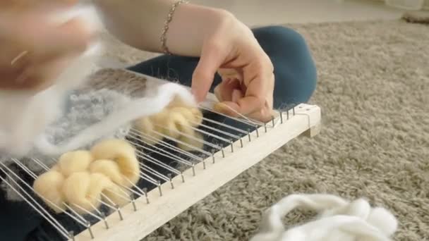 Eine Frau webt auf einem Webstuhl eine schöne Stickerei aus Garn, in einem heimischen Atelier, — Stockvideo