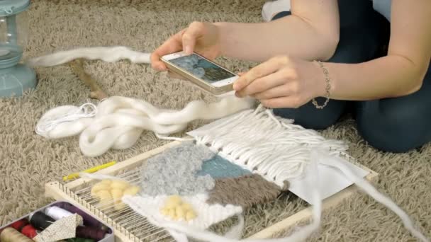 Žena spřádá na tkalcovském stavu krásnou výšivkou vyrobené z nití, v domácím studiu fotografie na telefonu — Stock video