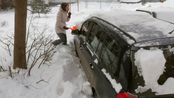 Молода жінка чистий автомобіль після снігового шторму зі скребком — стокове відео