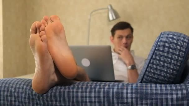 深刻なビジネス男性は物思いにふける、ノート パソコンでの作業、ソファの上に横たわる。足、クローズ アップ — ストック動画