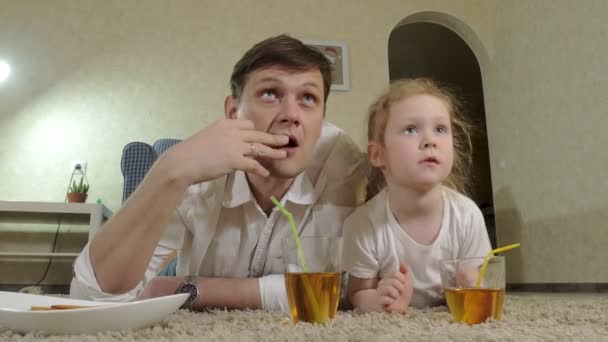 Man och dotter titta på TV, sitter på golvet dricka juice — Stockvideo
