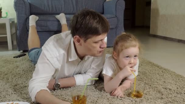 Hombre e hija viendo la televisión, sentado en el suelo beber jugo — Vídeo de stock