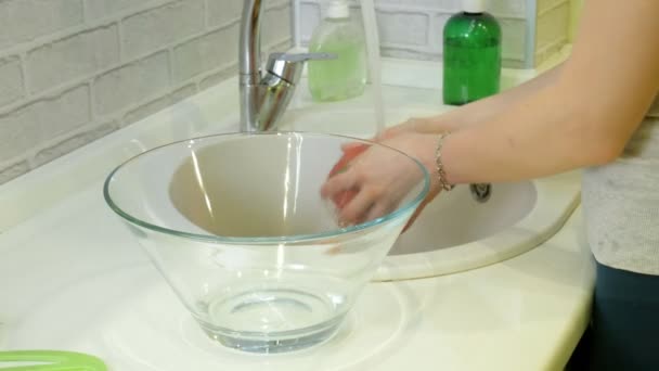 Vrouw wast verse groenten onder de kraan in de gootsteen in de keuken zet ze in een glazen beker — Stockvideo