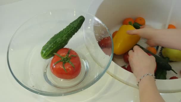 Kvinnan tvättar färska grönsaker under kranen i diskhon i köket sätter dem i en glas-kopp — Stockvideo