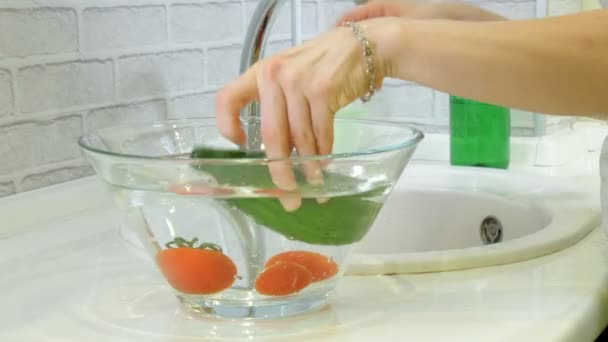Mulher lava legumes frescos sob a torneira na pia na cozinha coloca-los em uma xícara de vidro — Vídeo de Stock