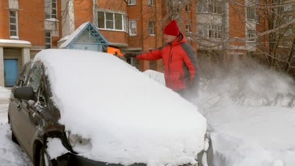 Чоловік чистий автомобіль після снігової бурі зі скребком — стокове відео
