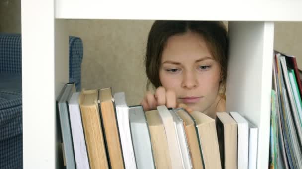 寻找一本书的年轻妇女。学生选择书架库。图书馆女书书架. — 图库视频影像
