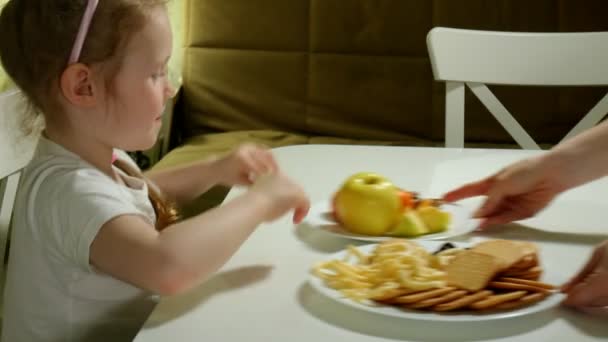 Hermosa chica dulce rechaza un plato de fruta, chocolate, patatas fritas, toma un plato de bocadillos, chocolate, patatas fritas — Vídeo de stock