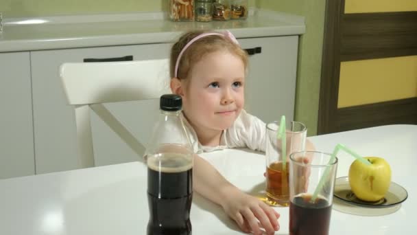 Cute little girl siedzi przy stole, wybiera to, co do picia, cola lub sok, pojęcie zdrowego stylu życia — Wideo stockowe